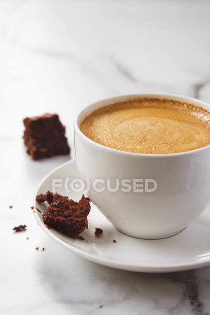 Brownie au chocolat en miettes sur une tasse de café latte et une soucoupe — Photo de stock