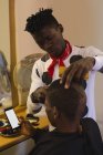 Cliente usando telefone celular enquanto barbeiro aparar seu cabelo na barbearia — Fotografia de Stock