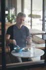 Geschäftsmann benutzt Handy beim Frühstück im Büro — Stockfoto