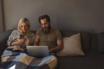 Couple using laptop and mobile phone in living room at home — Stock Photo