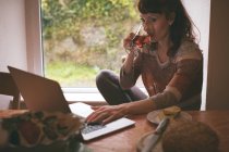 Жінка використовує ноутбук, маючи чашку чаю вдома — стокове фото