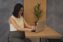 Embarazada mujer de negocios usando portátil en el escritorio en la oficina - foto de stock