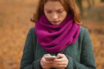 Жінка використовує мобільний телефон в парку восени — стокове фото