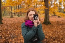 Женщина фотографируется с винтажной камерой в парке осенью — стоковое фото