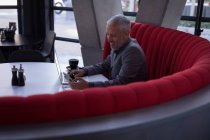 Uomo d'affari che utilizza il telefono cellulare mentre lavora sul computer portatile nella hall dell'hotel — Foto stock