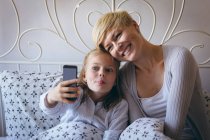 Mãe e filha tomando selfie com telefone celular em casa — Fotografia de Stock