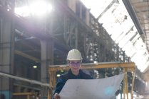Female technician looking at blue print in metal industry — Stock Photo