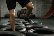 Section basse de l'homme musclé à l'entraînement de saut de pneu dans la salle de gym — Photo de stock