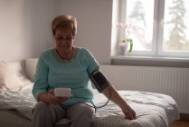 Seniorin überprüft Blutdruck zu Hause auf Monitor — Stockfoto