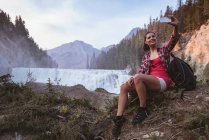 Young woman taking selfie with mobile phone near waterfall — Stock Photo