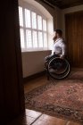 Disabled man in wheelchair looking through window at home — Stock Photo