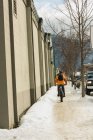 Rückansicht eines Mannes, der im Winter mit dem Fahrrad auf dem Gehweg fährt — Stockfoto