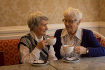 Amigos mayores interactuando entre sí mientras toman café en casa - foto de stock