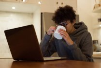 Красива жінка використовує ноутбук, маючи каву на кухні — стокове фото