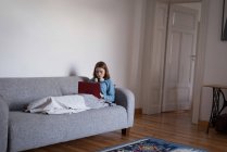 Mujer usando un portátil en el sofá en la sala de estar en casa - foto de stock