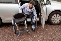 Behinderter junger Mann im Rollstuhl beim Einsteigen in sein Auto — Stockfoto