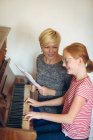 Sorridente madre che assiste la figlia nel suonare il pianoforte a casa — Foto stock