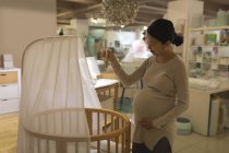 Щаслива вагітна жінка дивиться на дерев'яну колиску в магазині — стокове фото