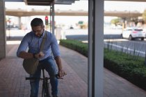 Чоловік дивиться на смарт-годинник під час їзди на велосипеді на тротуарі — стокове фото