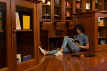 Jeune homme lisant un livre à la bibliothèque — Photo de stock