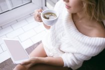 Жінка використовує цифровий планшет, маючи зелений чай вдома — стокове фото