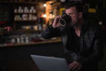 Mecânico usando laptop enquanto toma café na garagem — Fotografia de Stock