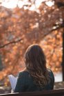 Rückansicht einer Frau, die im Park ein Buch liest — Stockfoto