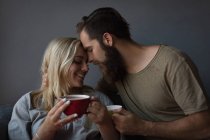 Пара обіймає один одного, маючи каву у вітальні вдома — стокове фото