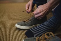 Section basse de l'homme attachant des lacets dans le salon à la maison — Photo de stock