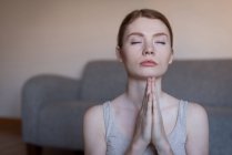 Jeune femme méditant avec les mains jointes dans le salon — Photo de stock
