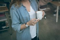 Ejecutiva femenina usando teléfono móvil mientras toma café en la oficina - foto de stock