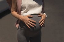Partie médiane de la femme enceinte touchant son ventre par une journée ensoleillée — Photo de stock