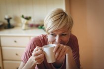 Улыбающаяся женщина пьет кофе дома — стоковое фото