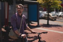 Uomo con bicicletta in piedi sulla strada in una giornata di sole — Foto stock