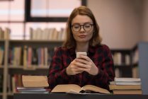 Jovem mulher usando um smartphone na biblioteca — Fotografia de Stock