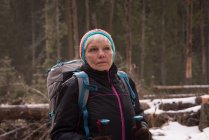 Nachdenkliche Seniorin steht im Winter mit Rucksack und Wanderstock — Stockfoto