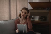 Frau nutzt digitales Tablet mit Kopfhörer zu Hause — Stockfoto
