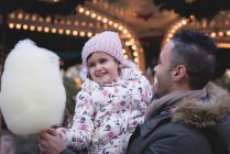 Padre e hija teniendo algodón de azúcar al atardecer en el parque de atracciones - foto de stock