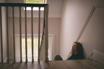 Mujer pensativa sentada en la escalera en casa - foto de stock