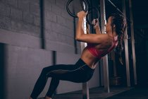 Fit femme tirant vers le haut sur les anneaux de gymnastique dans la salle de gym — Photo de stock