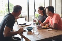 Бізнес-колеги обговорюють ноутбук під час сніданку в офісі — стокове фото