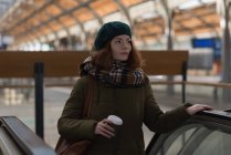 Женщина держит чашку кофе на эскалаторе на вокзале — стоковое фото