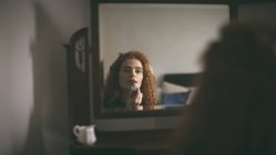 Женщина наносит помаду перед зеркалом дома — стоковое фото