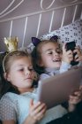 Geschwister mit Handy und digitalem Tablet auf Bett im Schlafzimmer — Stockfoto