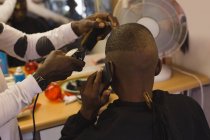 Cliente hablando por teléfono móvil mientras el peluquero se corta el pelo en la peluquería - foto de stock