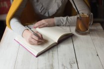 Mittelteil der Frau schreibt Notiz auf Buch mit Zitronensaft auf Tisch — Stockfoto