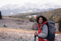 Donna premurosa in piedi con zaino e palo da trekking durante l'inverno — Foto stock