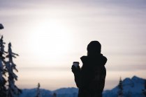 Frau mit Kaffee und Blick auf schneebedeckte Berge in der Abenddämmerung — Stockfoto