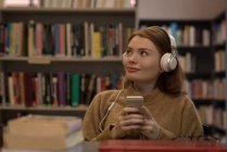 Jovem mulher ouvindo música na biblioteca — Fotografia de Stock