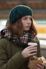 Mujer en ropa de invierno que tiene una envoltura y café en la estación de tren - foto de stock